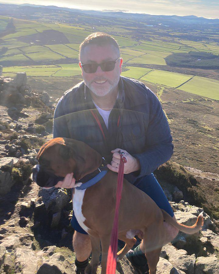 Damian and Buddy, the Pensionbuddy dog, on a hilltop above green fields.